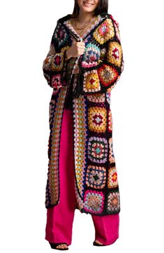 a woman in a colorful crochet coat and pink pants posing for the camera