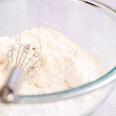 a glass bowl filled with flour and a whisk