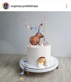 a birthday cake with a bear on top and bunting flags in the background, sitting on a wooden table