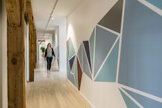 a woman walking down a hallway in front of a wall with geometric designs