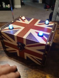 a wooden box with lights on it sitting on a table next to a person's hand