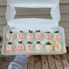 a person holding up a box filled with chocolate covered strawberries that spell out the word future mrs