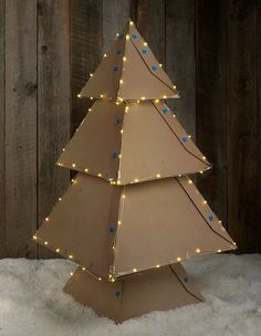 a cardboard christmas tree with lights on it in front of a wooden fence and snow