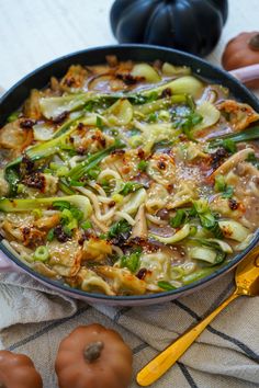 a pan filled with noodles and vegetables on top of a table next to pumpkins