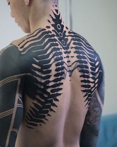 the back of a man's body with black and white tattoos on his chest