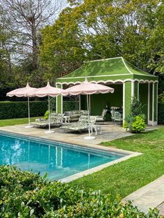 an outdoor pool area with lawn chairs and umbrellas near the swimming pool, surrounded by greenery