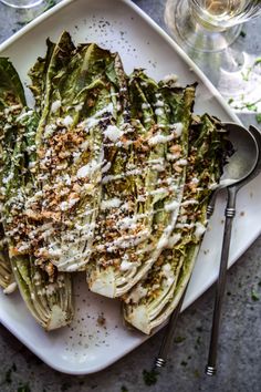 a white plate topped with lettuce covered in cheese and seasoning next to wine glasses