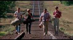 three people standing on the side of a train track with luggage bags in their hands