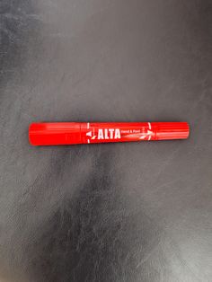 a red pen sitting on top of a metal table next to a black surface with the word ata written on it