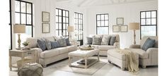 a living room filled with white furniture and lots of windows on top of the walls