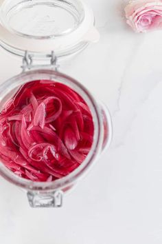 a jar filled with red onions sitting on top of a table next to pink flowers