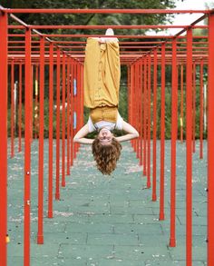 a woman is upside down in the middle of some red metal structures with her hands on her head