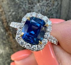 a woman's hand holding an engagement ring with a blue sapphire surrounded by diamonds