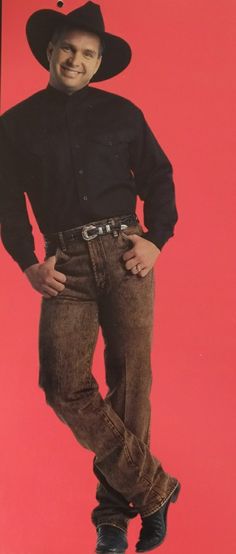 a man in cowboy hat and jeans standing with his hands on his hips against a red background