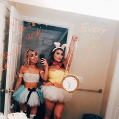 two women dressed up in bunny ears and tutus taking a selfie with a clock