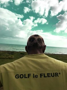 a man in yellow shirt flying a kite near the ocean on a sunny day with blue sky and clouds