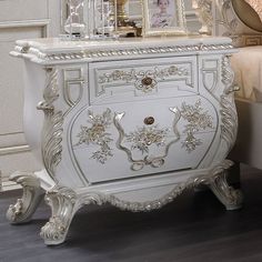 an ornate white cabinet with gold trimmings on the drawers and doors, in front of a bed