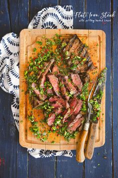 steak with herbs on a cutting board next to a knife and fork in the foreground