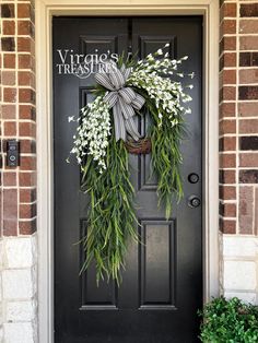 a black front door with a wreath and white flowers hanging on it's side