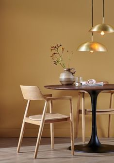 a dining table with two chairs and a vase on top of it, in front of a yellow wall