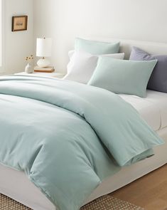 a bed with blue sheets and pillows in a white room next to a wooden floor