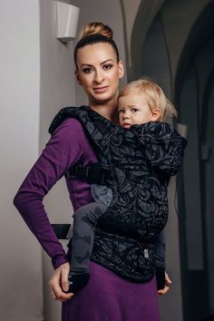 a woman is holding a baby in a black and purple wrap on her back,