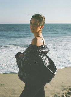 a woman walking on the beach with a black jacket over her shoulders and an ocean in the background