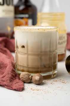 a glass filled with liquid next to some nuts and cinnamons on a counter top