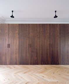 an empty room with wooden cupboards and lights on the ceiling above it is a parquet wood floor