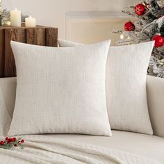 two white pillows sitting on top of a couch next to a christmas tree with red ornaments