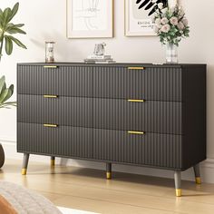 a black dresser with yellow handles in a white room next to a potted plant