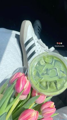 some pink tulips are next to a cup with green liquid