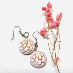 two white and brown earrings sitting next to pink flowers