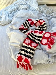 a red and black scarf laying on top of a bed next to a pillow,