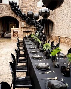 a table set up with black balloons and place settings for an elegant dinner party in front of a brick building