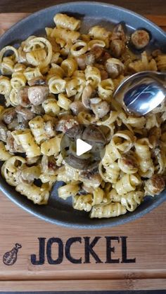 a bowl filled with pasta and mushrooms on top of a wooden table next to a spoon