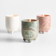 three different colored candles sitting next to each other on a white surface with one candle in the middle