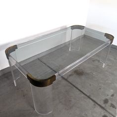 a clear glass table with gold trim around the edges and bottom, sitting on concrete flooring