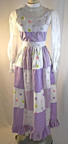 A Super nice and very cute lavender and white themed patchwork gingham, calico, and embroidered multi colored daisies fabrics.  The bib has a wide scoop neckline.  It is lined with the lavender floral calico fabric and the straps are also made of the calico.  The straps are stitched to the back waist.  The waistband and ties are made of the calico fabric.  The skirt is full, lined with white cotton and with a pleated gingham and solid lavender patchwork flounce at the hem.  The only flaw I can find are two pale blue drip marks (about 1 inch by 1/4 inch on the lining fabric.  The marks do not go through to the outer fabric.  Sorry about the wrinkles on the bib, I was in a hurry to take the pictures.  I'll press the pinafore before shipping.  The bib is 12 1/2 inches wide at the bust, the wa Colored Daisies, Blue Drip, Calico Fabric, Lavender Floral, Bib Apron, Prairie Style, In A Hurry, Lining Fabric, Pale Blue