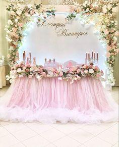 a table with pink tulle and flowers on it in front of a white backdrop