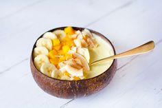 a wooden bowl filled with fruit on top of a white table next to a spoon