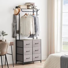 a bedroom with a bed, desk and hanging clothes on the rack in front of a window