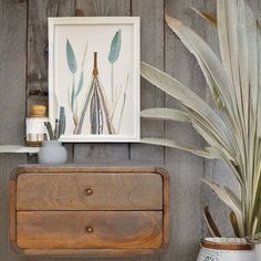 a wooden dresser with some plants on top of it and a framed picture above it