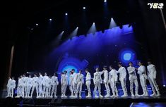 a group of men standing on top of a stage next to each other in white suits