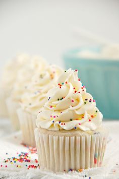 three cupcakes with white frosting and sprinkles on a table