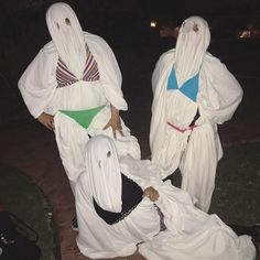 three people dressed in costumes sitting on the ground at night with one person laying down