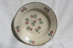 a white bowl with red and green flowers on the rim sits on a white cloth