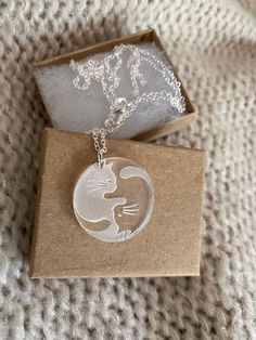 a necklace with a cat on it sitting in a cardboard box next to a chain