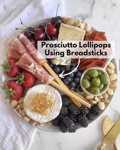 a platter filled with cheese, meats, fruit and crackers on top of a white table