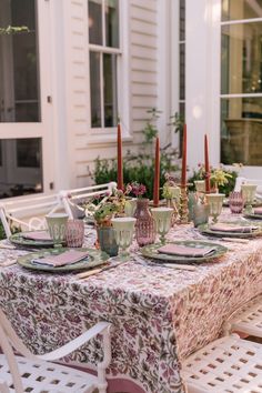 the table is set with plates, cups and vases on it in front of a white house